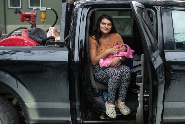 A woman holding a baby sits in the back of a truck.