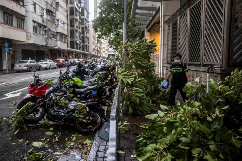 A pedestrian navigates a sidewalk littered with fallen tree branches. 