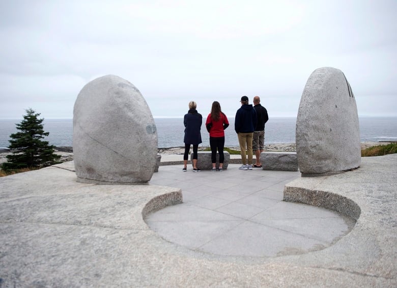 Four adults stand between two large boulders overlooking the ocean. 