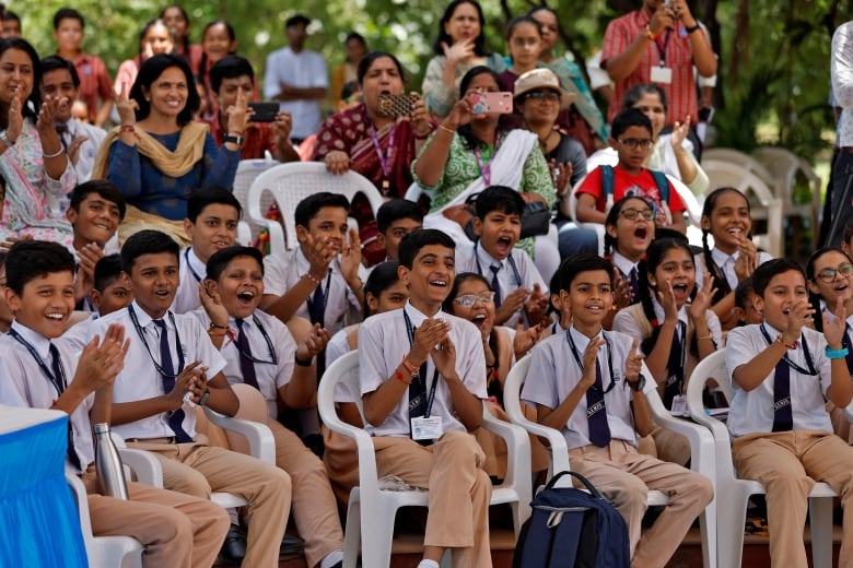 Rows of seated children smile and cheer. 