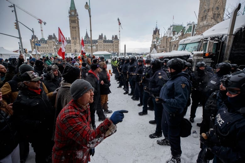 A photo of protesters and police standing face to face in Ottawa, with the parliament building in the background.