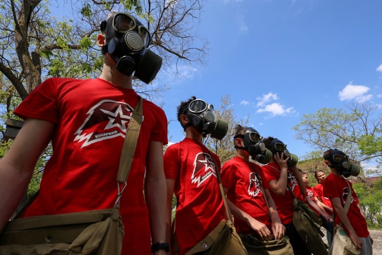 Teenagers in red T-shirts wear gas masks.