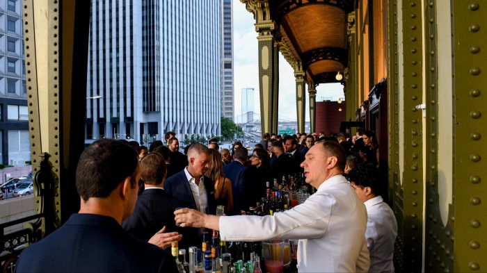 Manhattanites drink at a bar with a view over skyscrapers