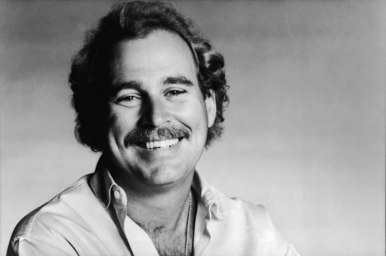 A black and white photograph of a man with a moustache smiling for the camera. 