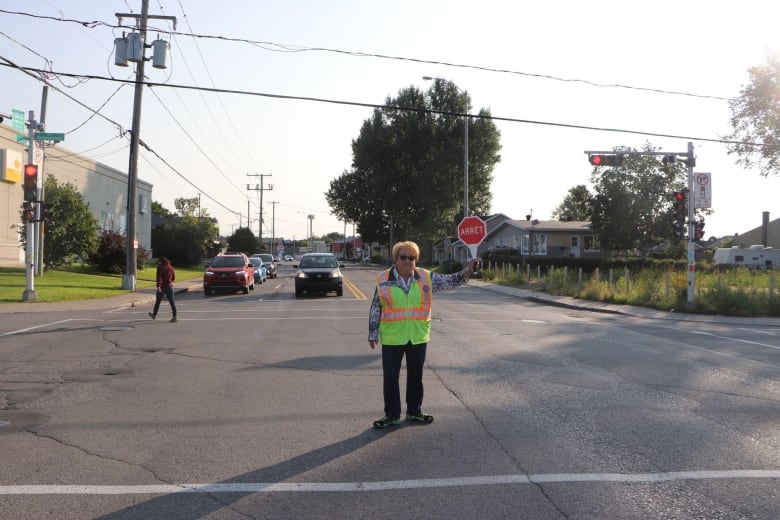 A woman stands in a yellow vest in an intersection with a stop sign. 