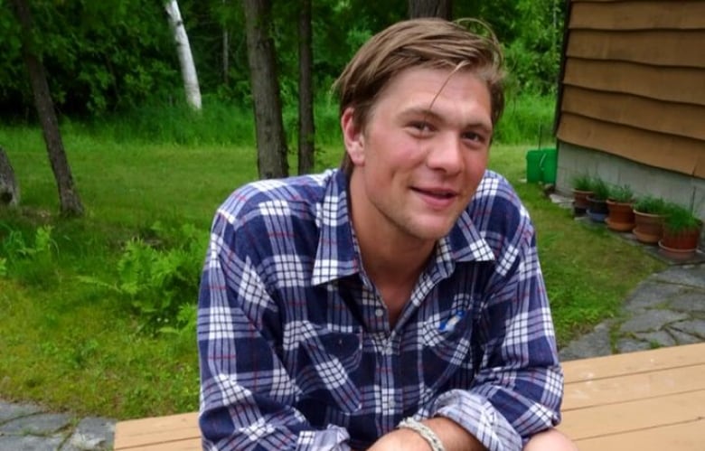 Young man sitting on picnic table smiling for camera