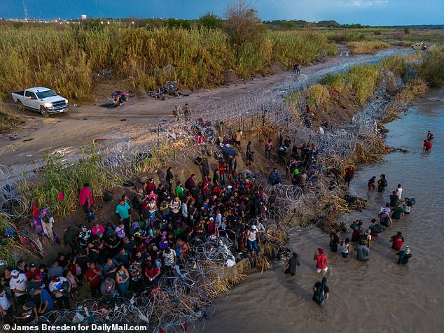 Moment groups of migrants creep through unguarded barbed wire at Eagle Pass under cover of darkness, skip the processing area and disappear into the woods