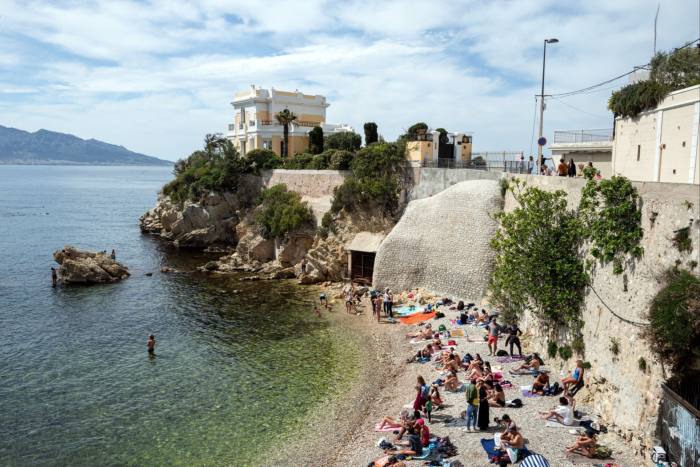 Sunbathers on a rocky beach under a seawall