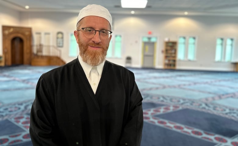 An imam stands in the prayer area of a mosque. 