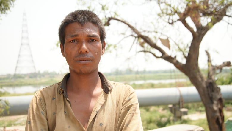 a man stands in front a pipeline, with a tree off to the side.