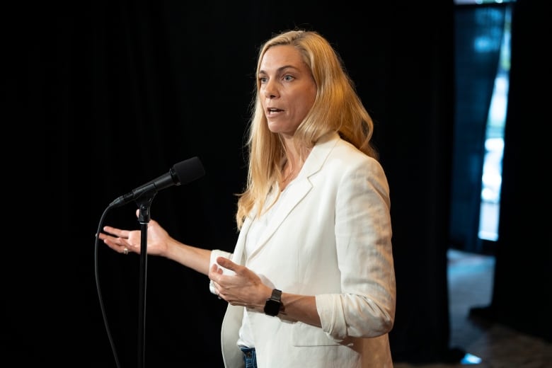 A woman in a white suit stands at a microphone.