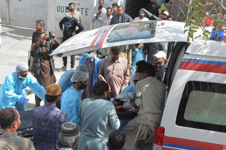 Health workers in scrubs stand at the back of a vehicle as a person is wheeled out.