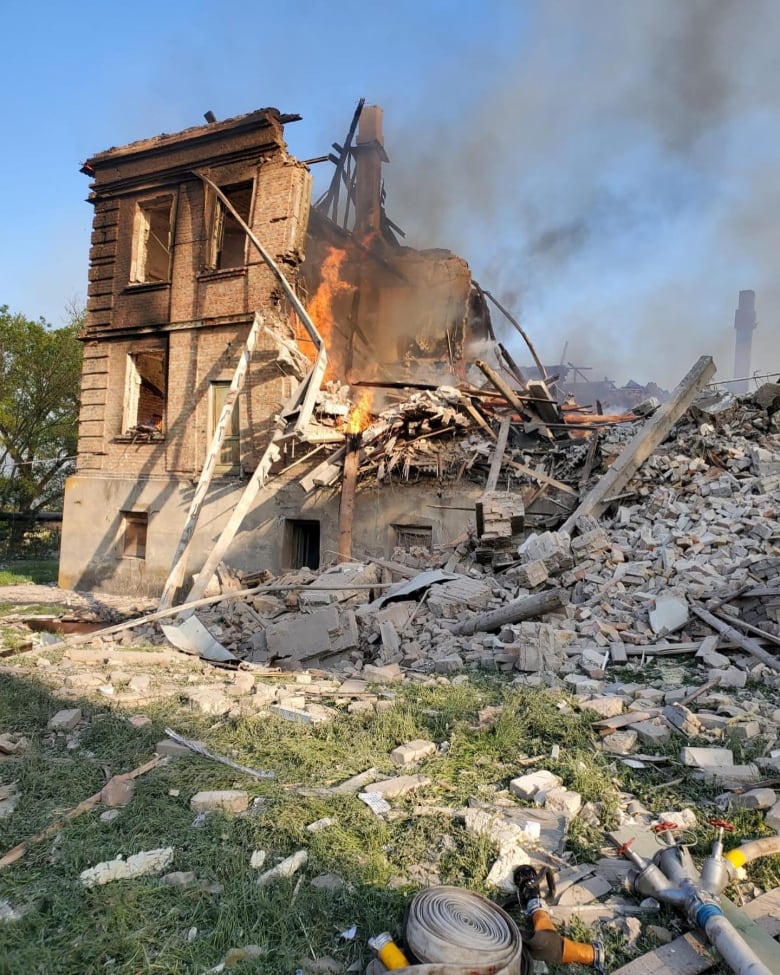 Flames and smoke rise from a destroyed building, with just one wall still standing