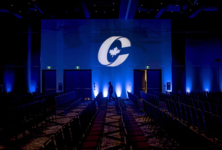 A man is silhouetted walking past a Conservative Party logo.