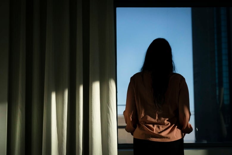  Woman stands in shadow in front of a window.