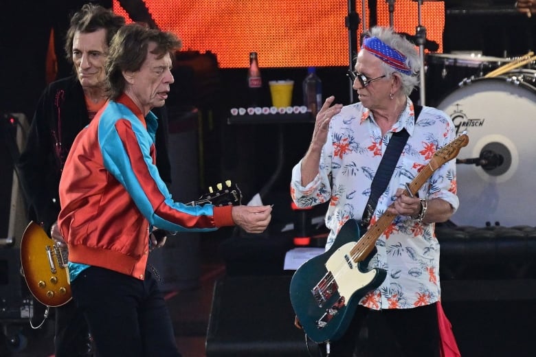 Three men are shown performing on stage, with two holding guitars.