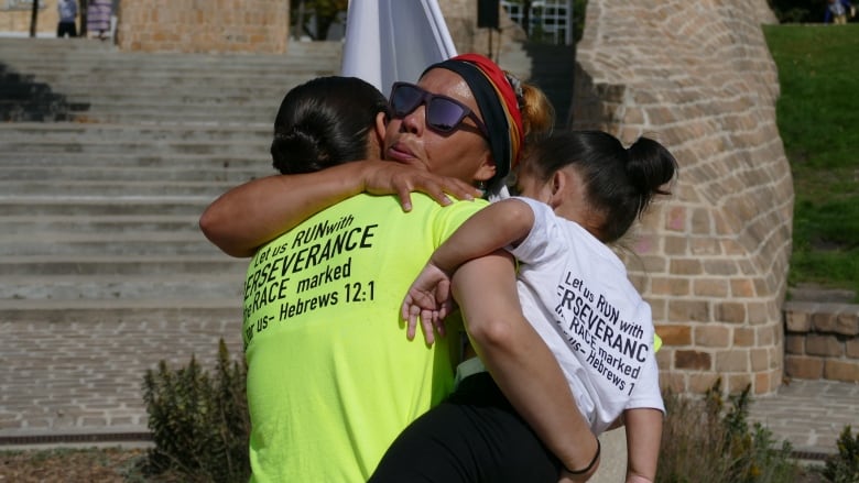 A woman in a white shirt hugs a woman in a yellow shirt. 