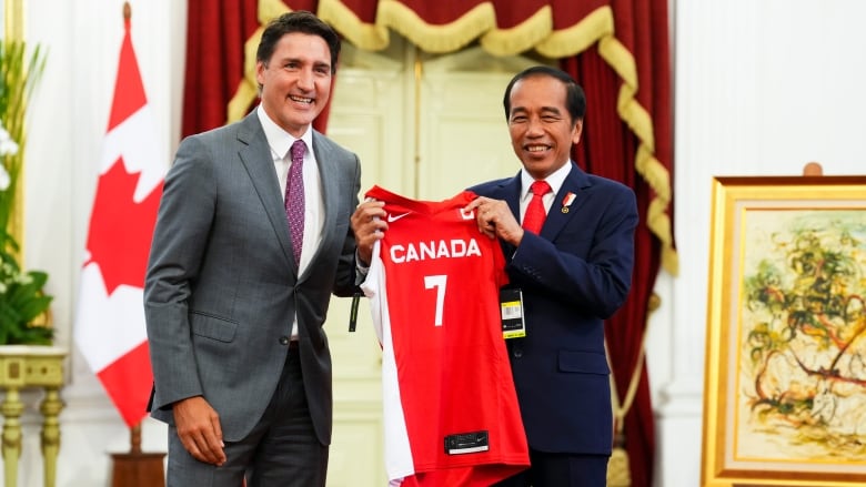 Two men in suits stand holding a basketball jersey and smiling for the camera.