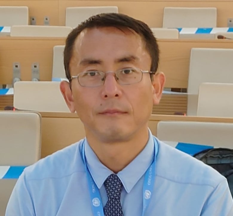 A man wears glasses and a blue shirt and tie.