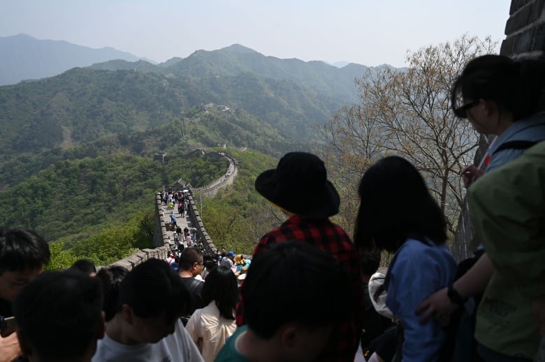 Several people are shown walking a long pathway seen cutting through mountains.