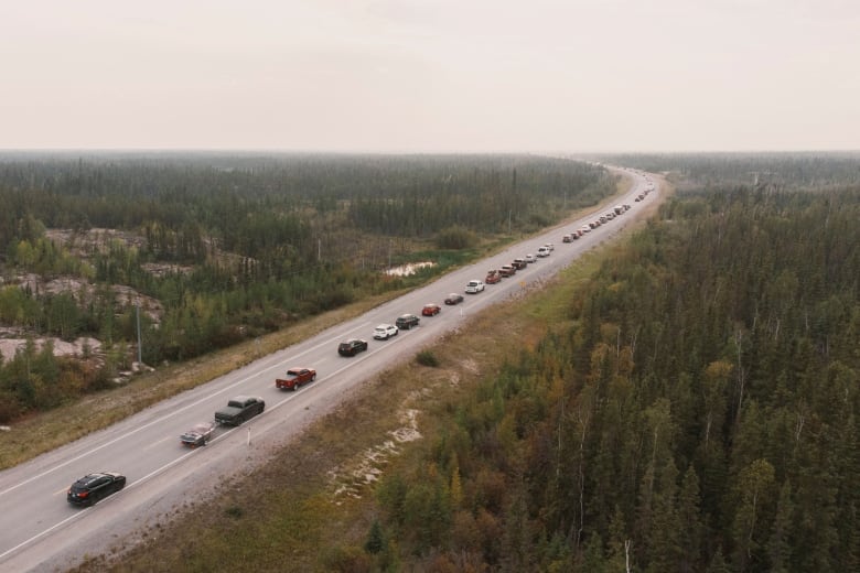 A long line of cars is seen driving in one direction on a rural highway.