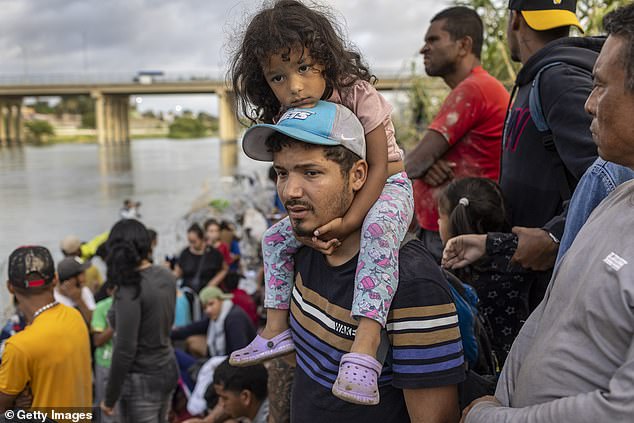 A man and child from Venezuela wait to be processed by US agents after crossing the Rio Grande into Eagle Pass