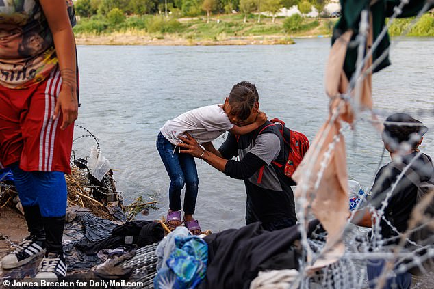 A young girl hugs someone as she makes it across the Rio Grande onto US territory in Eagle Pass, Texas