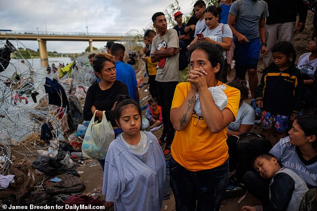 Migrants wait on the US-side banks of the Rio Grande to be processed after moving past feet of barbed wire. The wire, initially installed by Texas National Guardsmen, has mostly been cut away by Border Patrol agents