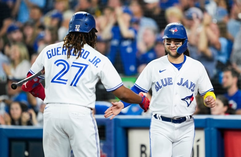 Two male baseball player slap their right hands together in celebration on the field.