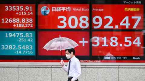 A man walks past an electronic board showing the numbers on the Tokyo Stock Exchange along a street in Tokyo