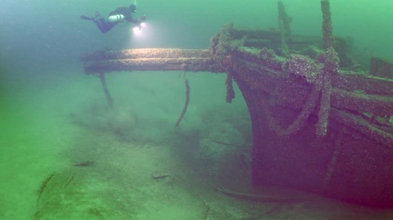 A diver with a flashlight underwater looking at a sunken ship