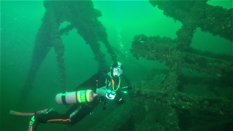 A scuba diver underwater exploring the paddlewheel of a wrecked steamer from 1812.