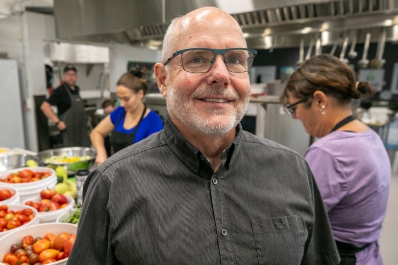 A man wearing a gray button down in shown in an industrial kitchen.