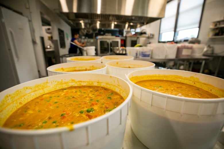 Large plastic tubs of soup are shown in an industrial kitchen.