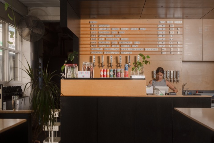 A woman behind the bar at Faculty. Behind her, on a large wooden board are listed the