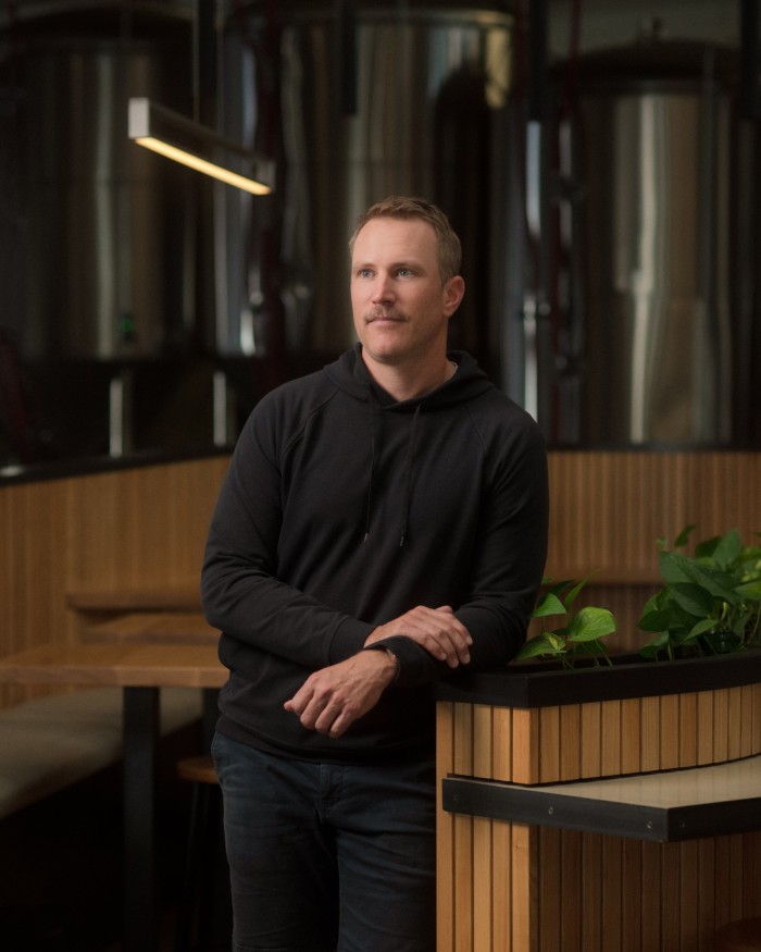 Superflux co-founder and president Adam Henderson leaning against a blond-wood planter, in front of tables and steel vats