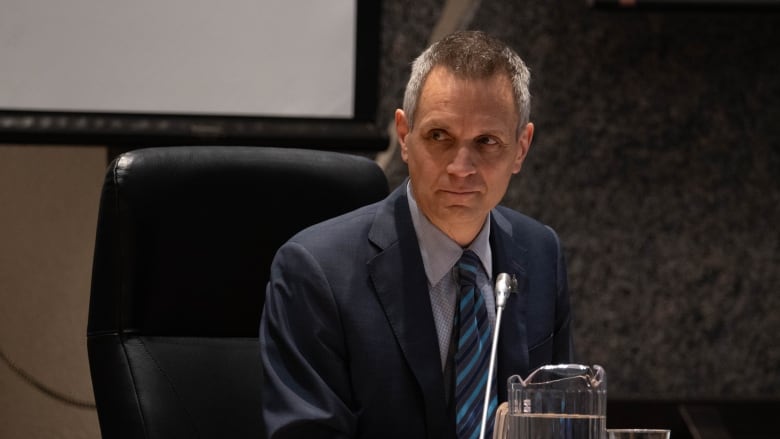 Man in a blue suit sits at a table with a jug of water