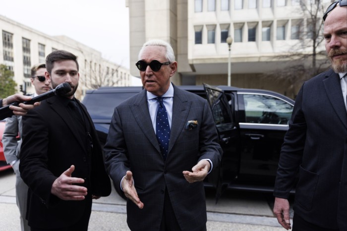 Roger Sone walks from a car, wearing dark suit and tie and sunglasses