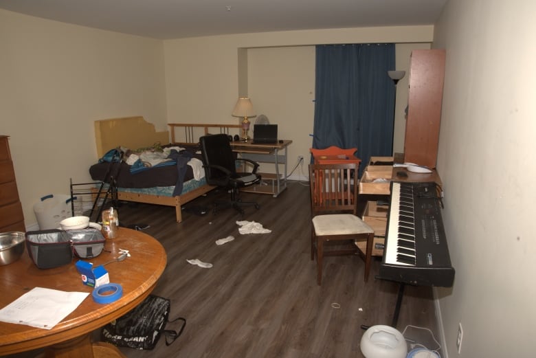 A photo of Nathaniel Veltman's downtown London apartment. It is a small bachelor apartment with clothes strewn on the floor and on the bed, and drawers in a chest of drawers open. 