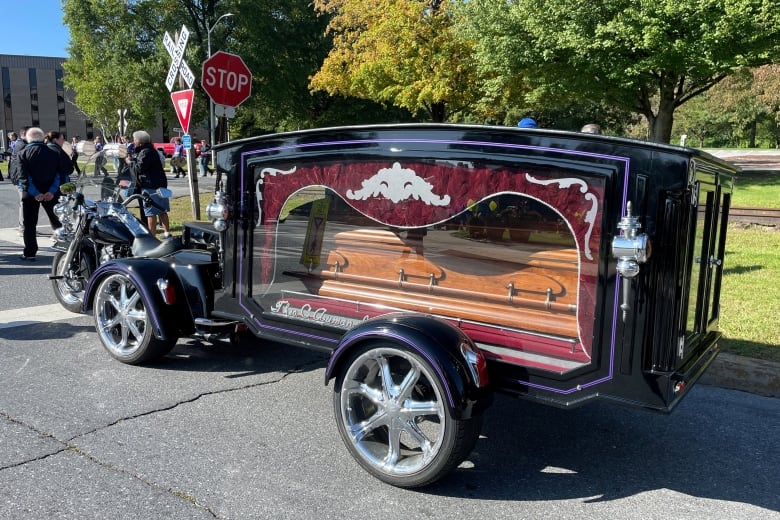 A brown coffin visible through a large display window in an ornate black hearse. 