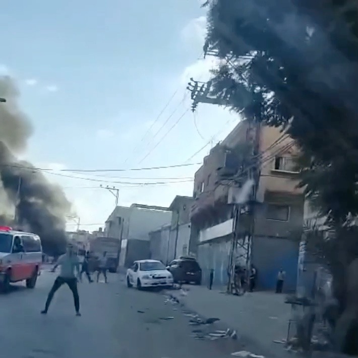 Sirens blare as an ambulance speeds down a wide street towards two cars on fire. As they approach, people on the street wave for attention