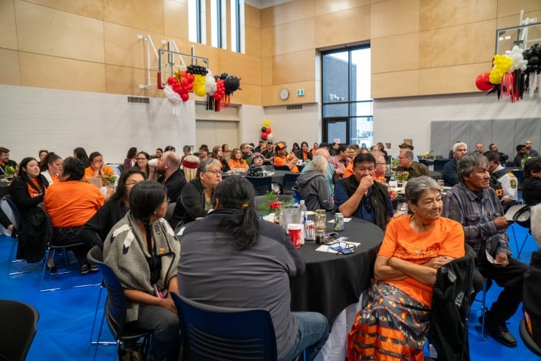 A crowd shot of people sitting at tables in a gym.