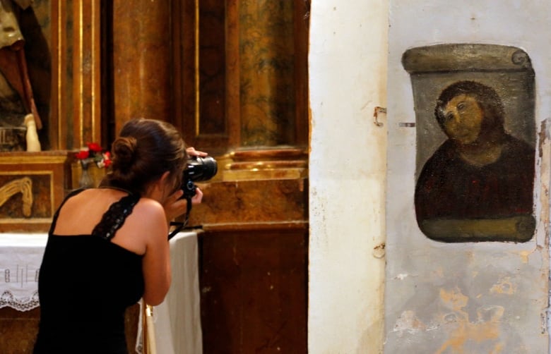 A young woman with brown hair snaps a photo of the botched restoration of a 19th-century painting of Christ.  