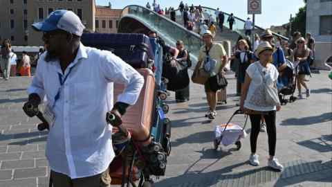 a porter with a cart full of suitcases by the Calatrava Bridge in Venice