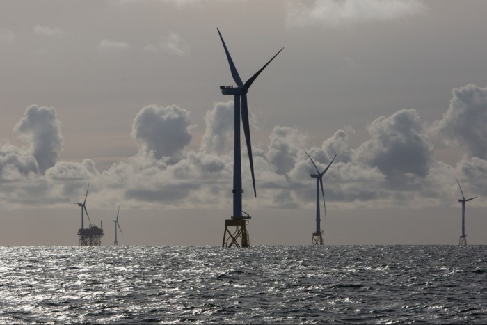 View of silhouetted wind turbines in the distance with sparkling sea in the foreground