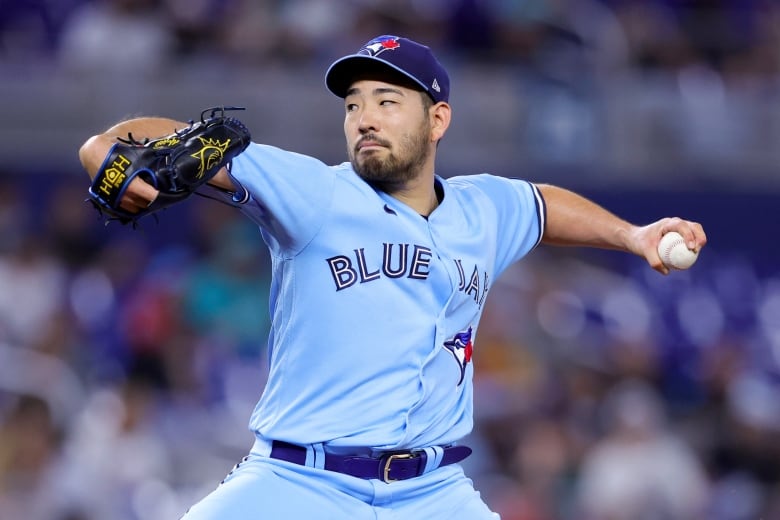 A baseball pitcher wearing a light blue Toronto Blue Jays uniform is seen mid-throw.