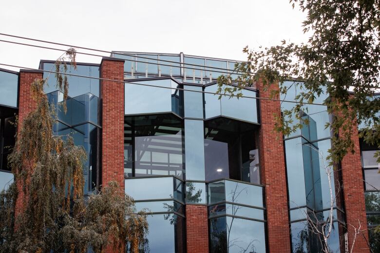 The upper part of a glass and brick building is shown against a cloudy sky.