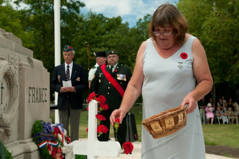 A woman places a red carnation on a white cross. She wears a dress with a poppie pinned on it.