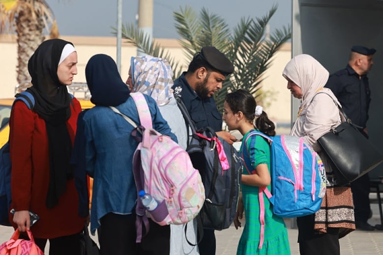 Women carrying backpacks line up in front of a man in uniform.