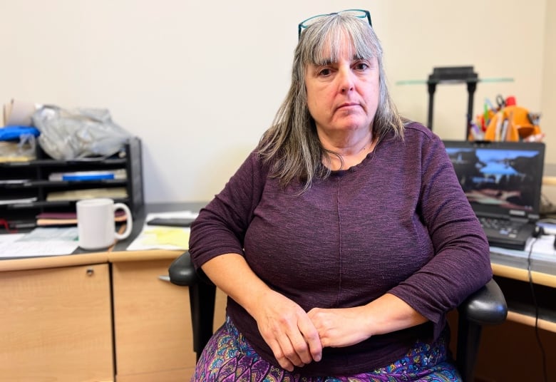 A woman in a purple shirt sits in a desk chair in an office. 